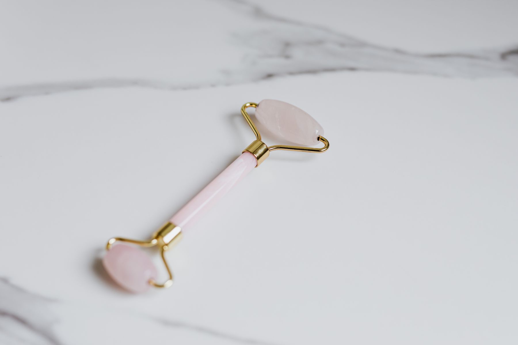 Rose quartz facial roller resting on cool marble